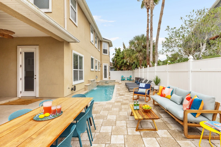 Luxurious Vilano Villa backyard with a pool, outdoor seating, colorful cushions, and tropical trees in St. Augustine.