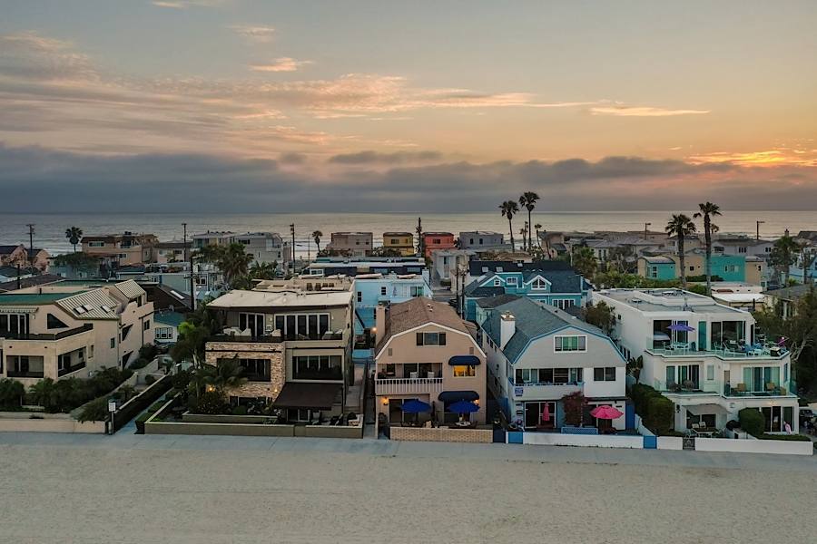 Colorful beachfront houses with ocean views, palm trees, and a sunset sky, perfect for luxury vacation rentals and golf access.