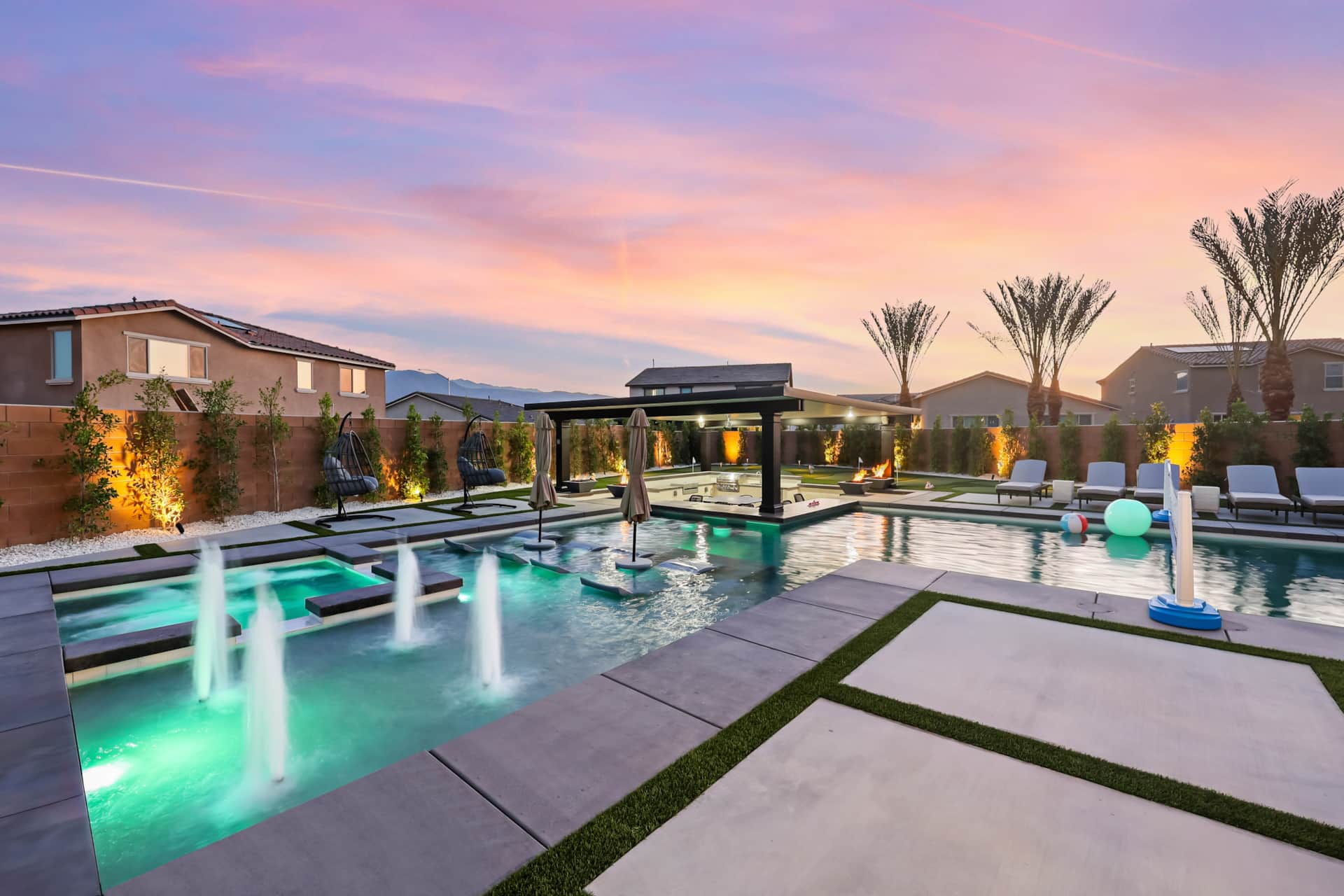 Luxurious desert resort pool area with swim-up bar, hot tubs, lounge chairs, and colorful floating balls at sunset.