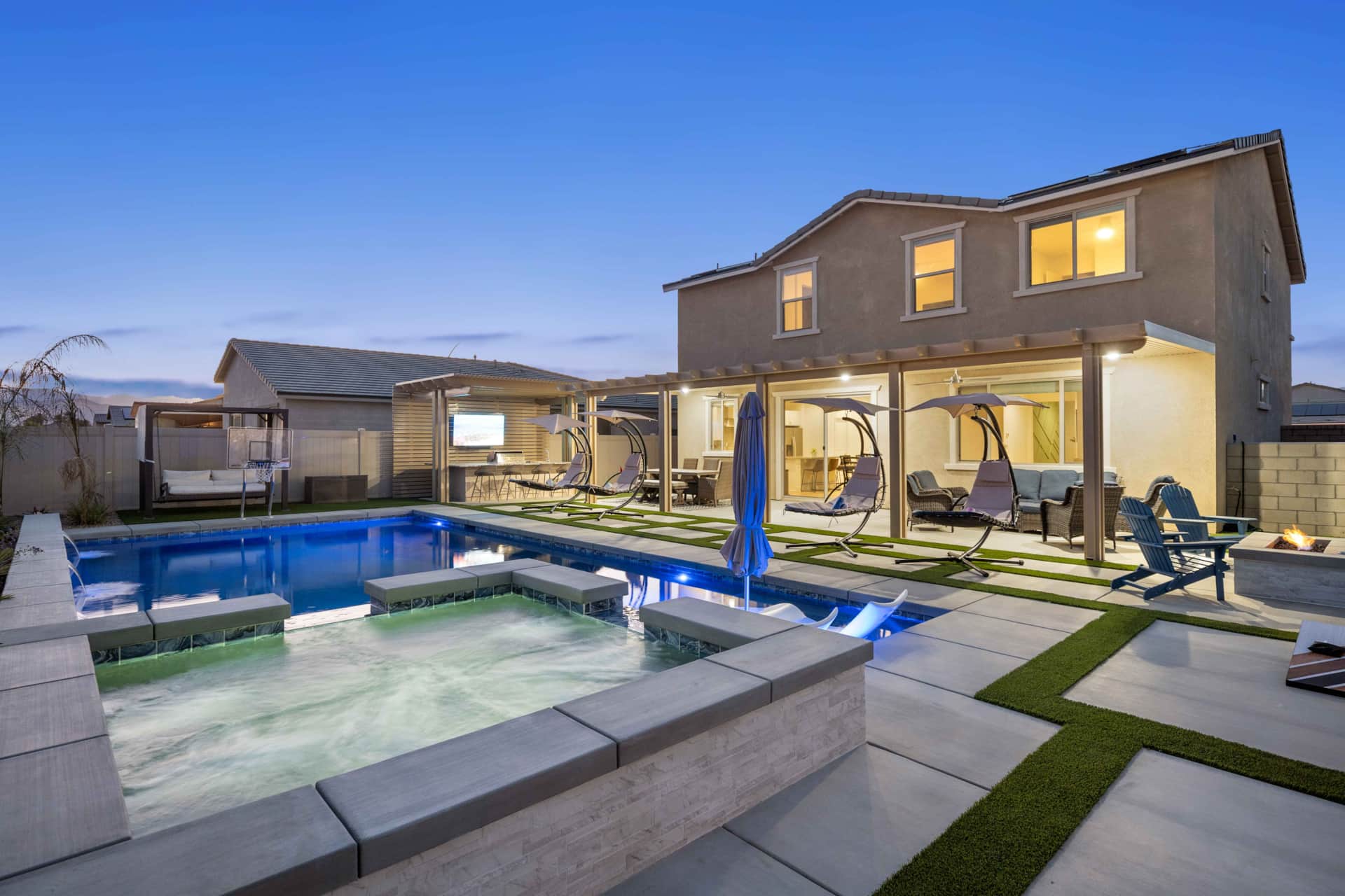 Luxury backyard with a swimming pool, hot tub, outdoor seating, hanging chairs, and a fire pit at dusk, part of a 6-bedroom resort.