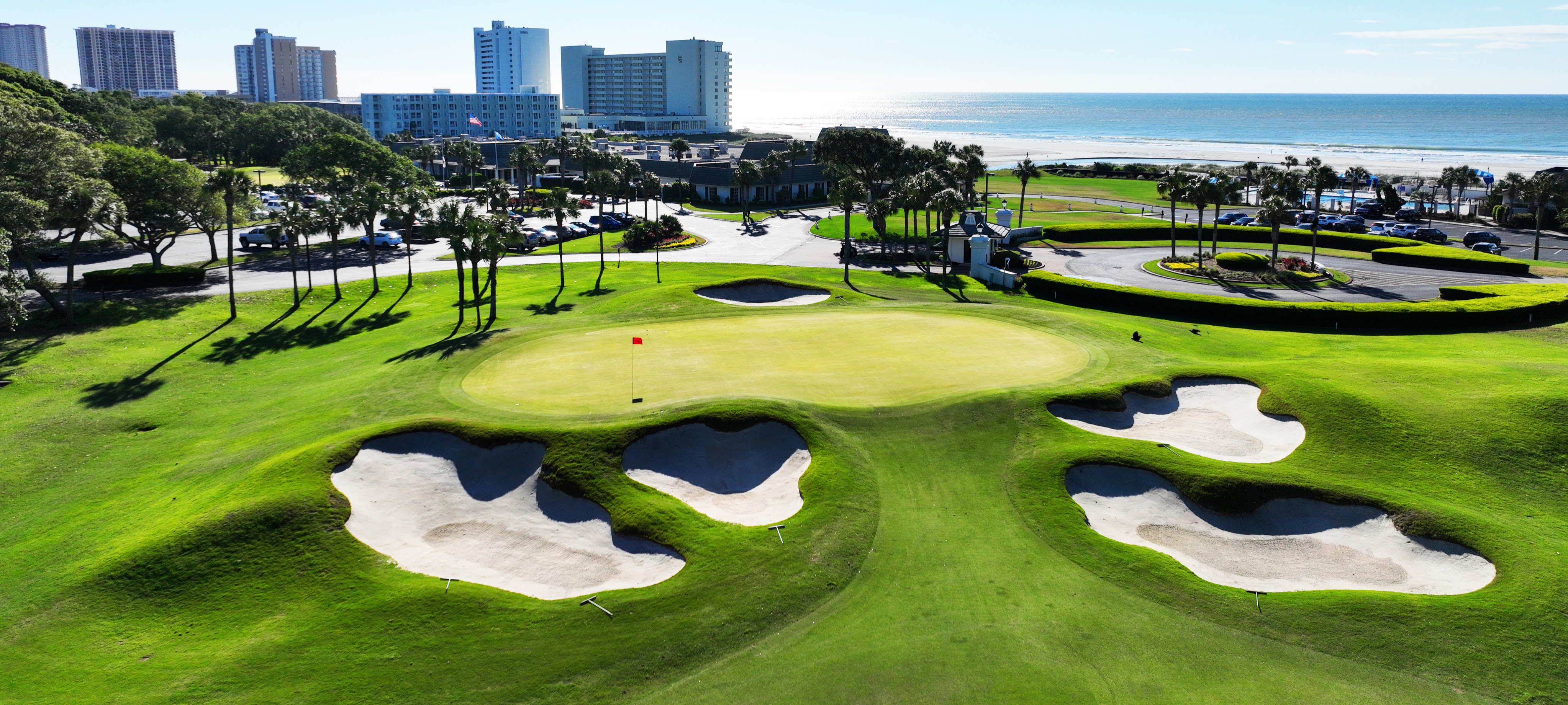 A scenic view of a Myrtle Beach golf course with sand traps, green fairways, palm trees, and ocean in the background.