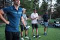 Group of four golfers preparing for a game on a lush golf course with trees and golf carts in the background, planning a golf trip.