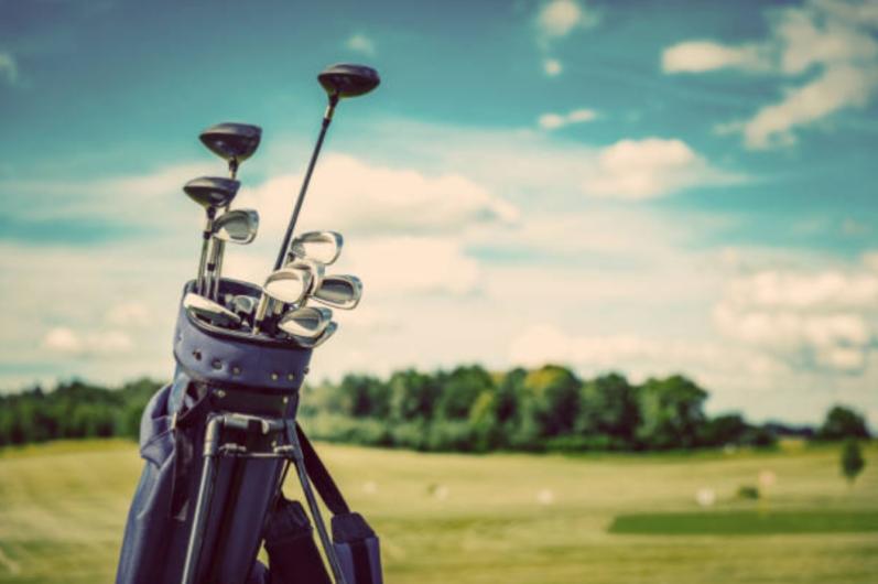 Golf clubs in a bag on a golf course, with a blue sky and clouds, illustrating a guide to renting golf clubs across the US.