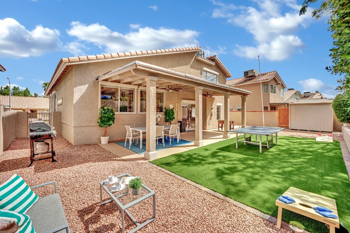 Bright backyard of a 4-bedroom rental home with a covered patio, outdoor dining, ping pong table, and landscaped yard.