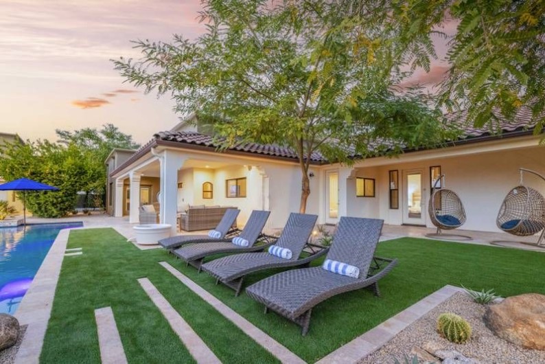 Luxurious Scottsdale vacation home with a pool, lounge chairs, and outdoor seating, surrounded by lush greenery at sunset.
